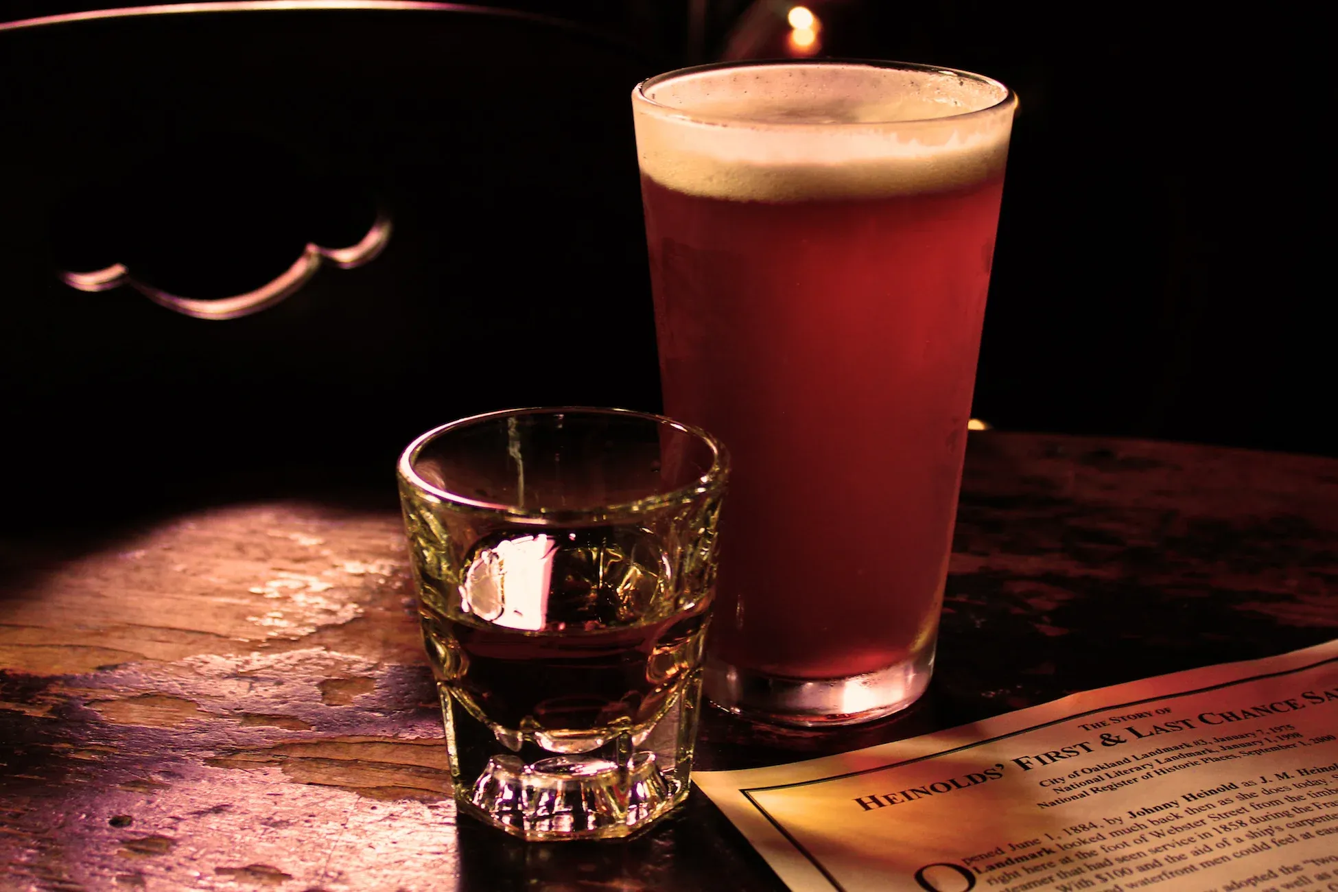 Red beer, shot, Heinold's Saloon paper on dark wooden table.