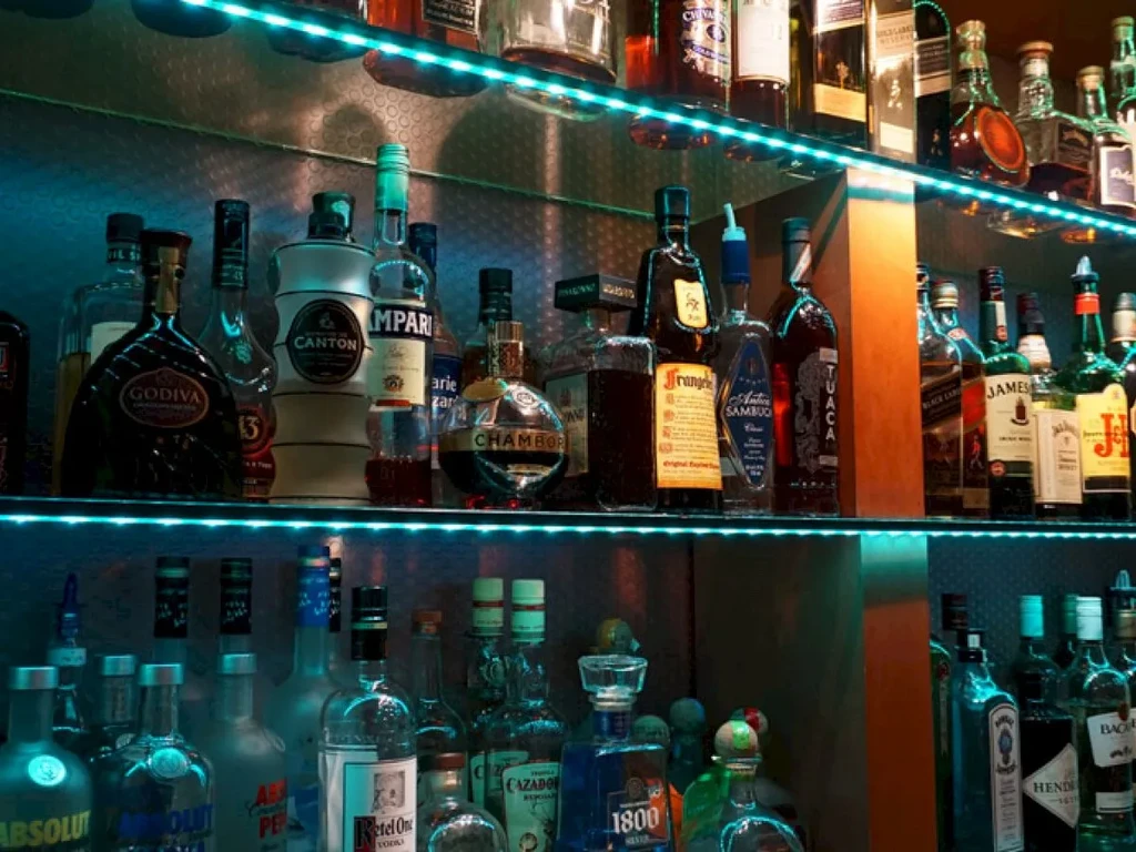 Three shelves filled with liquor bottles in a dimly lit bar.