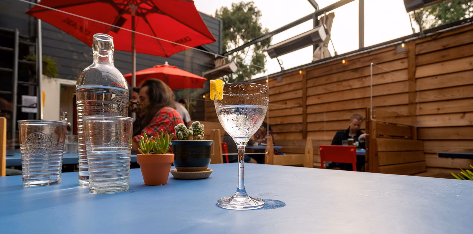 A chilled drink, water, and succulents on a blue outdoor table.