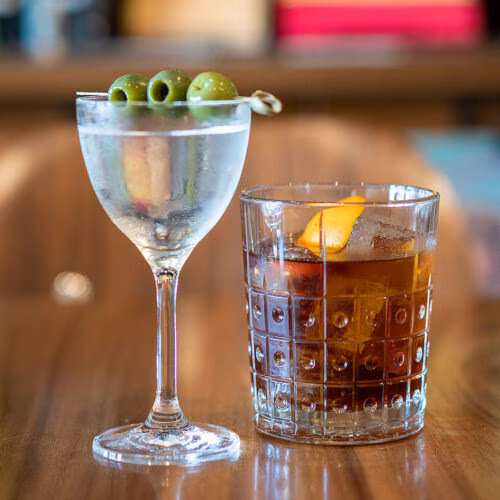 Martini with olives and a dark cocktail with orange peel.