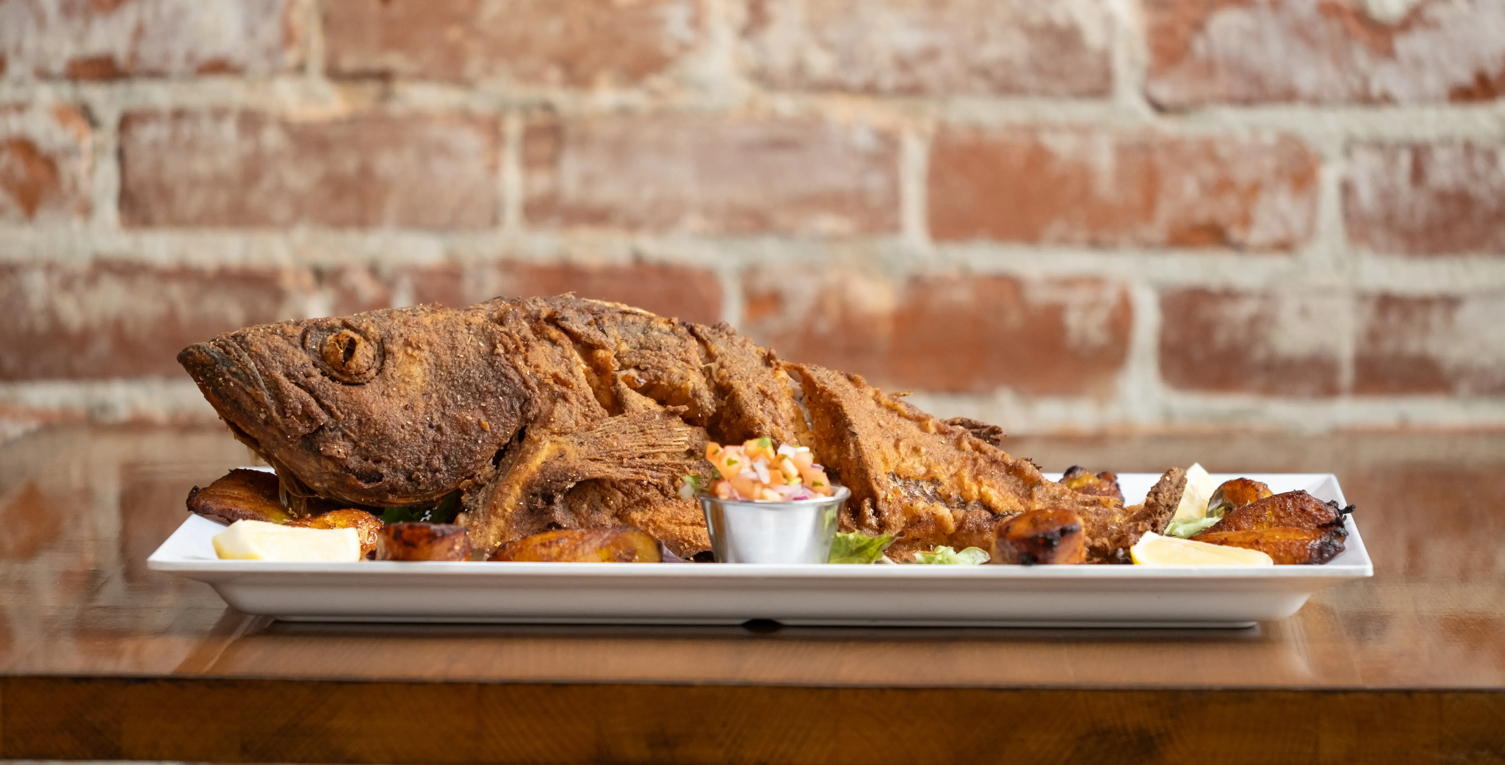 Deep-fried whole fish with plantains, lemon, and salsa.