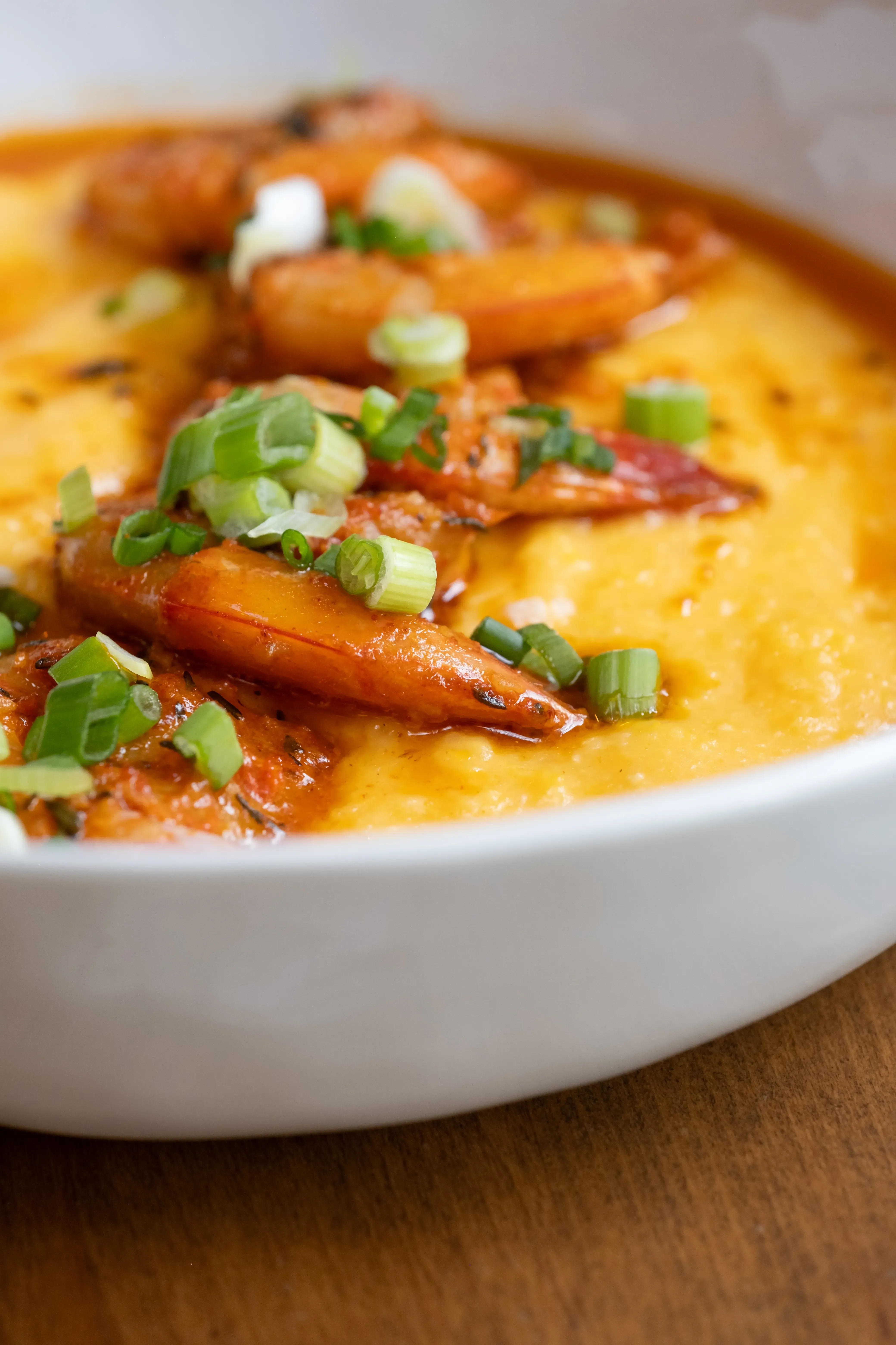 Shrimp and creamy yellow dish topped with green onions in a white bowl.