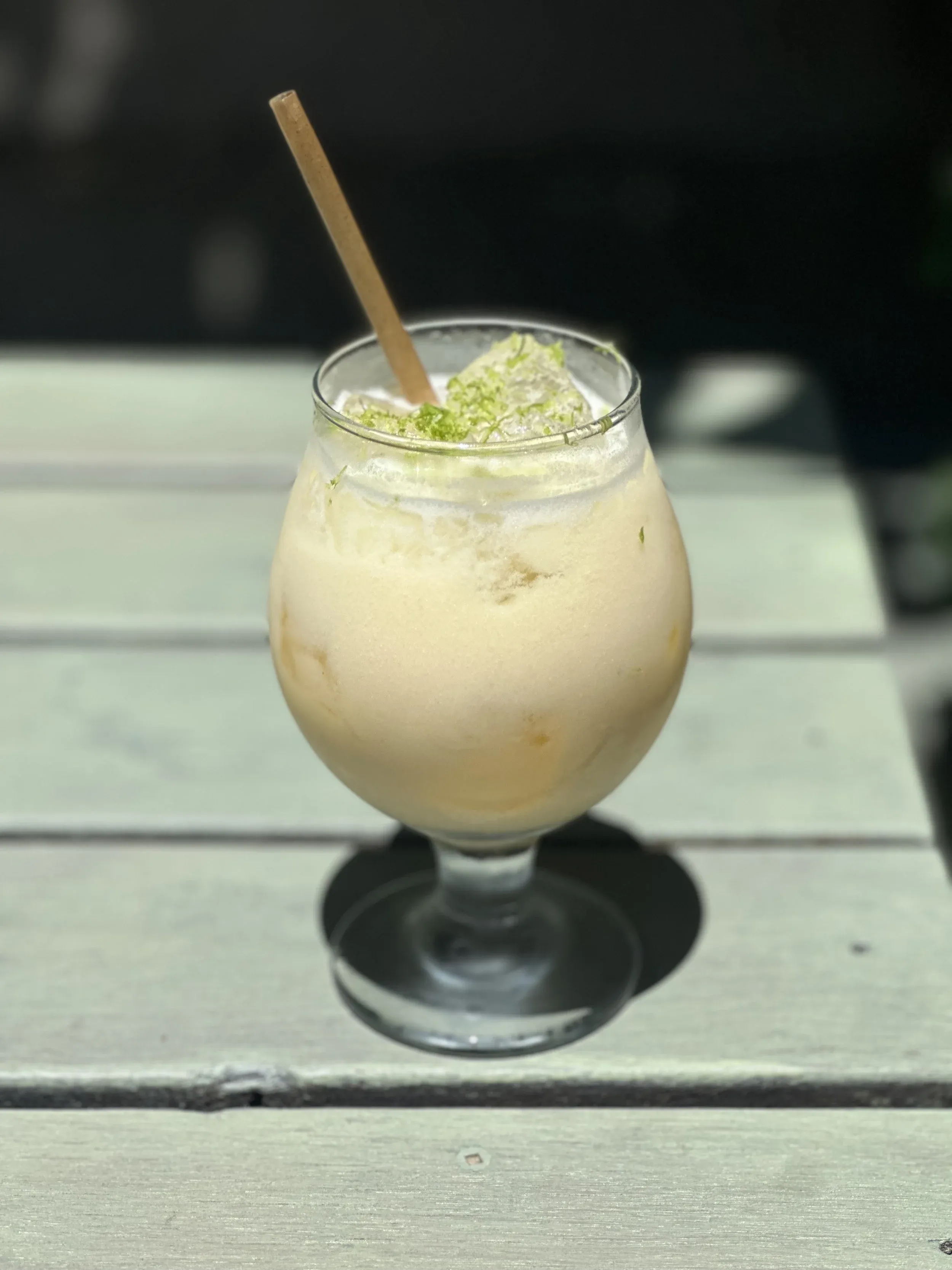 Light-colored frozen drink with frothy top, green zest, and straw.