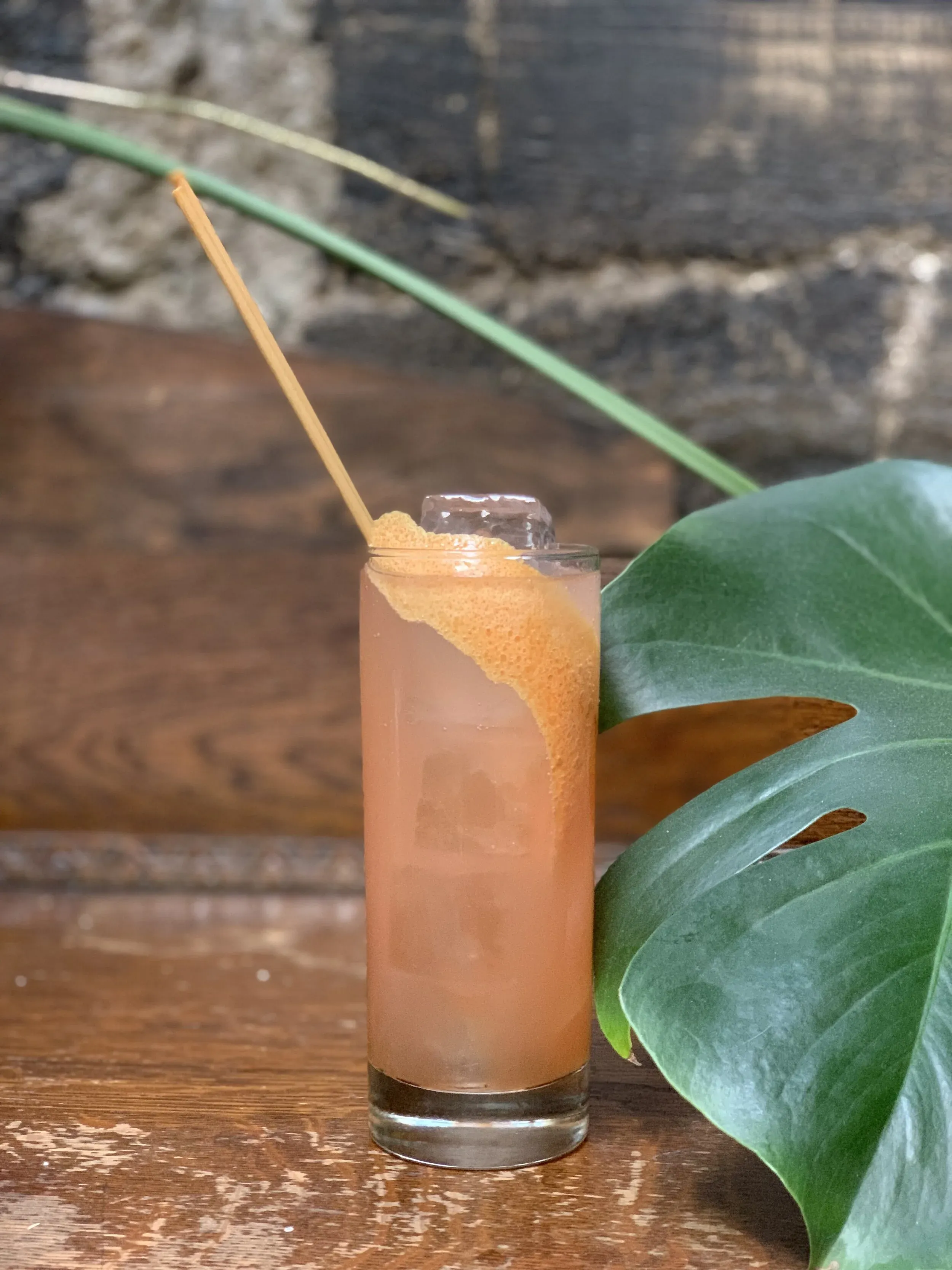 Pink drink with ice, orange peel, and straw on a wood surface.