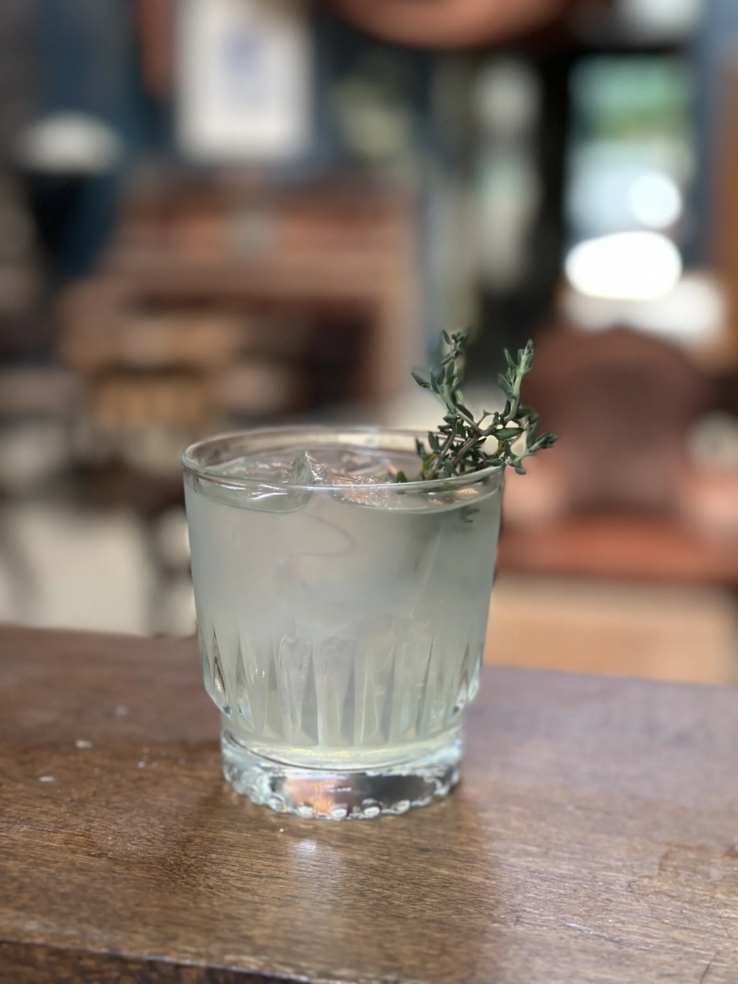 Faceted glass with clear drink, ice, and herb sprig.
