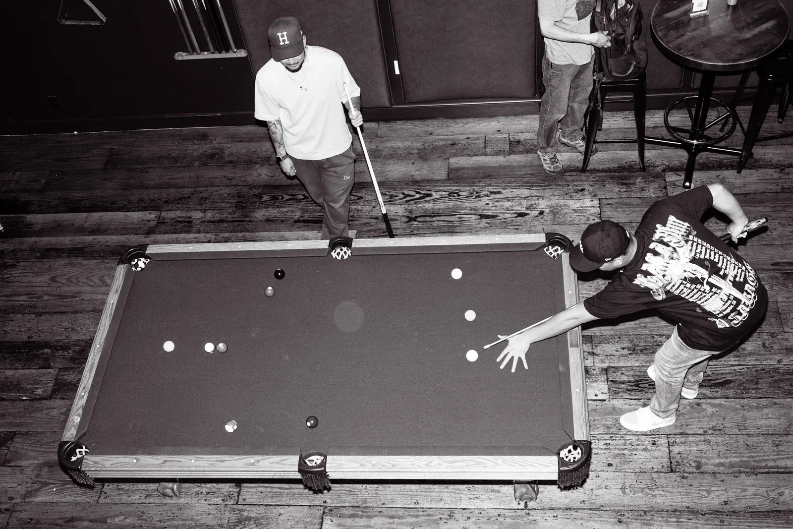 Black and white image of men playing pool, one shooting.