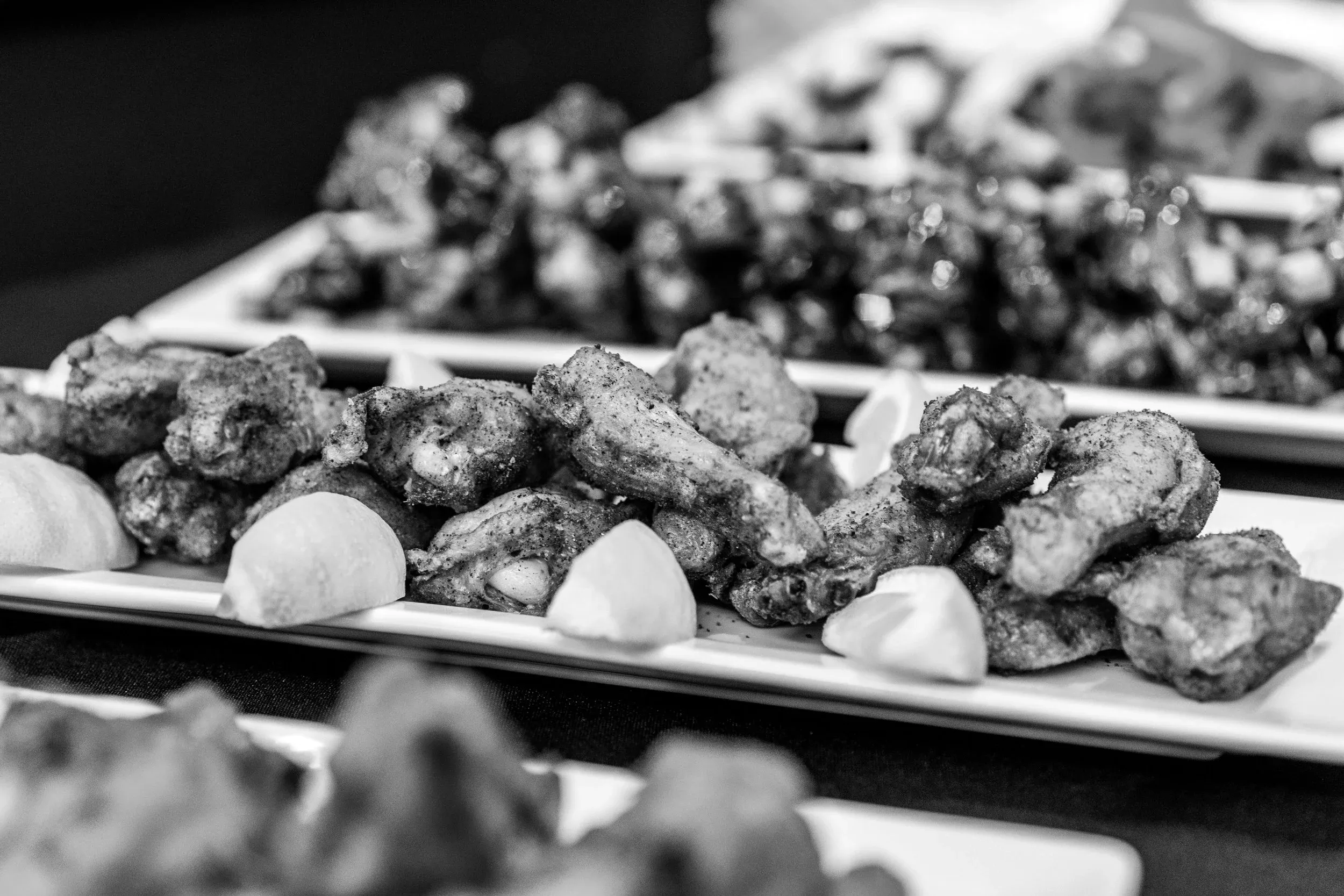 Black and white image of seasoned chicken wings with lemon wedges.