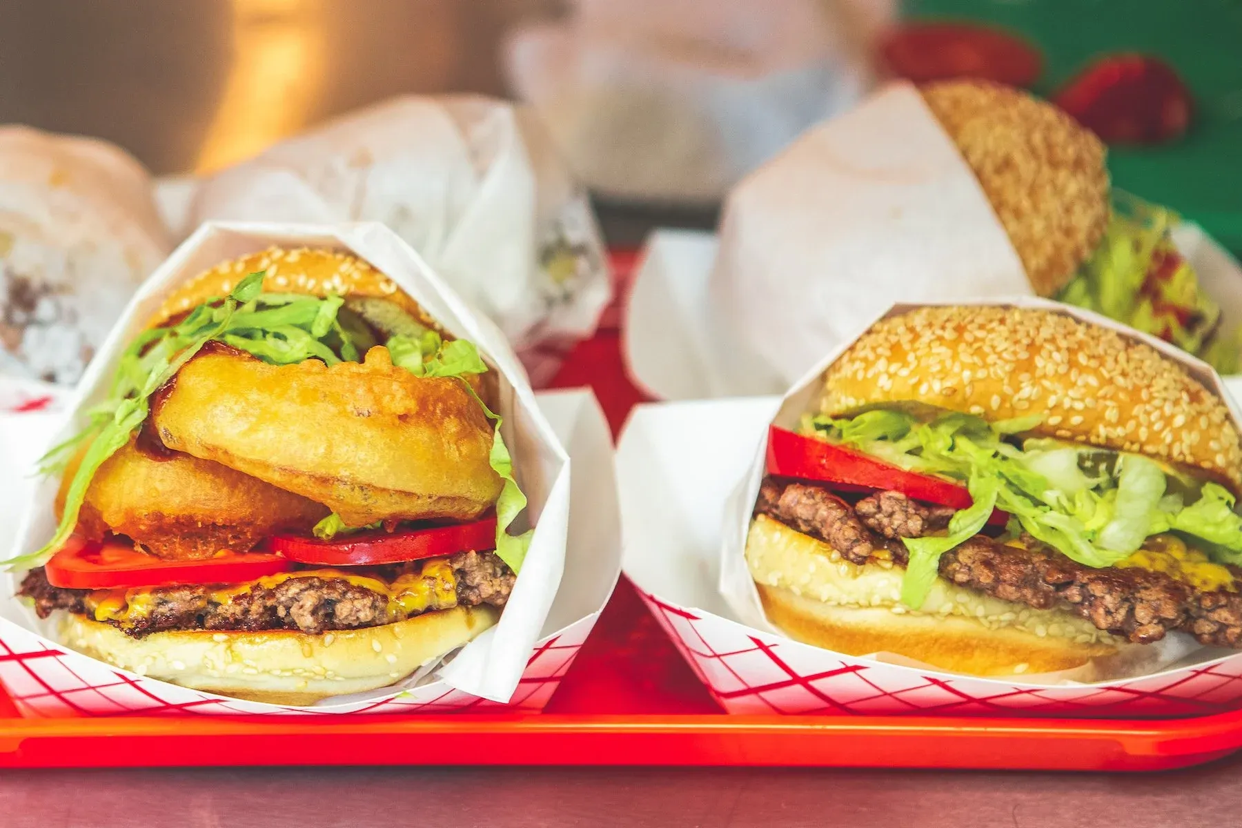 Two burgers, one with onion rings, lettuce, tomato, cheese.