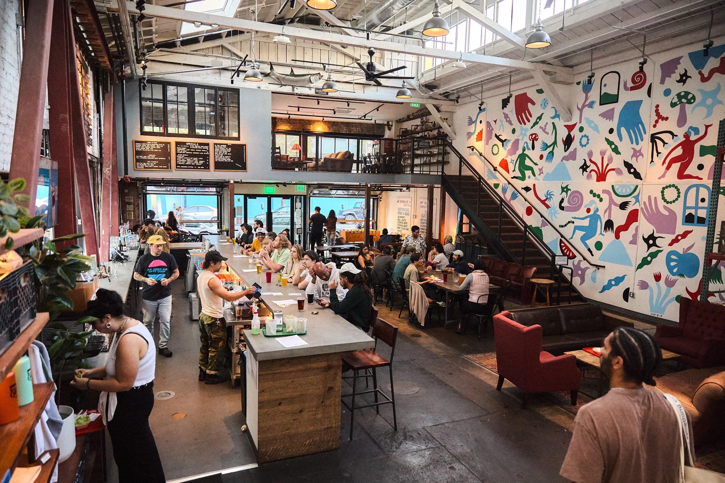 Large, open restaurant interior with a bar, diners, and colorful mural.