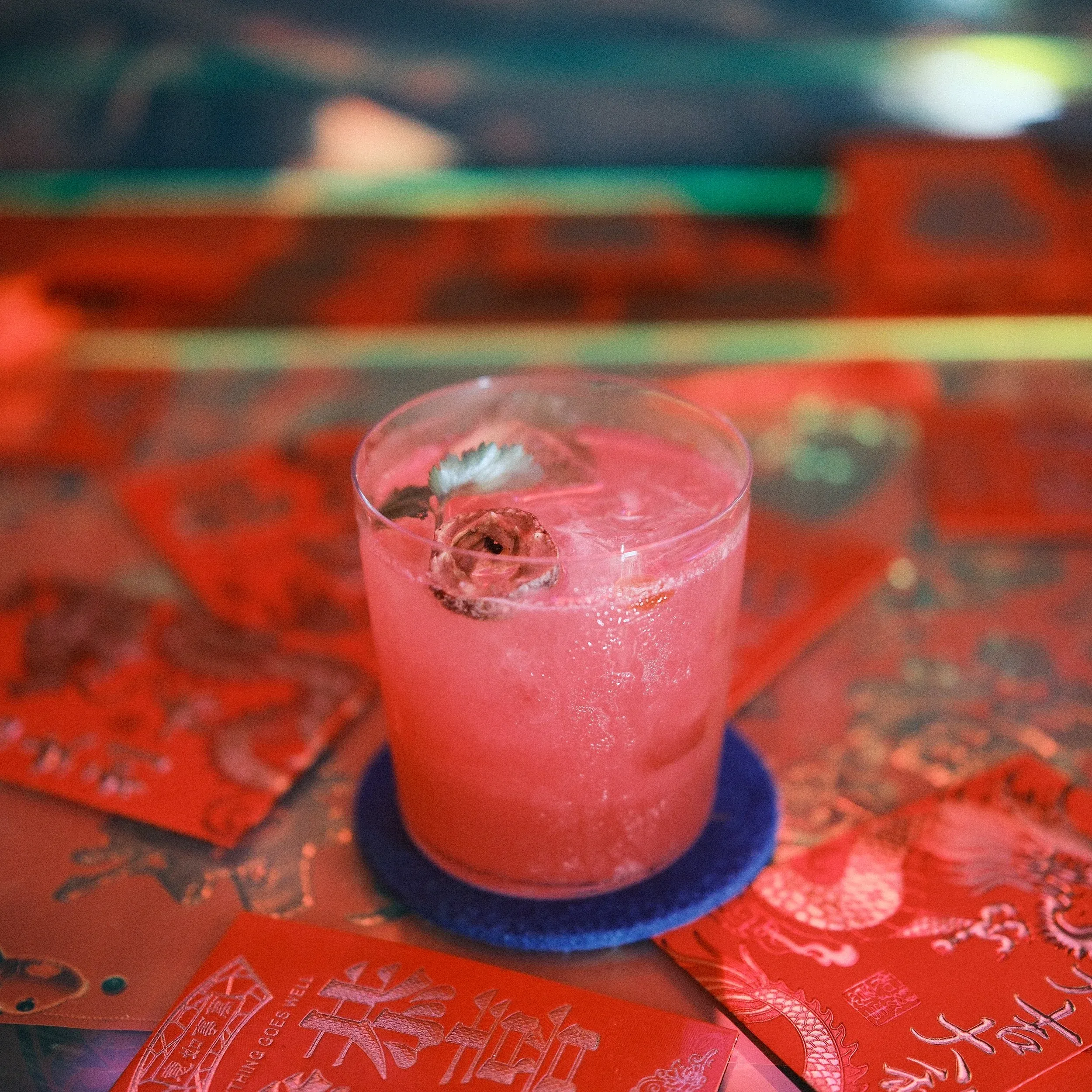 Pink cocktail with dried flower garnish surrounded by red envelopes.
