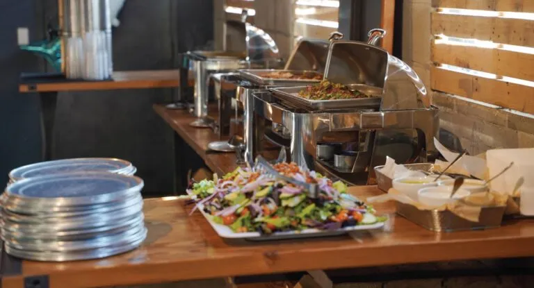 Buffet table with chafing dishes, a large salad, and plates.