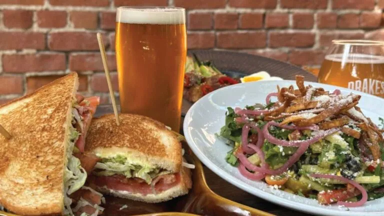 Toasted sandwich, colorful salad, and two beers against a brick wall.