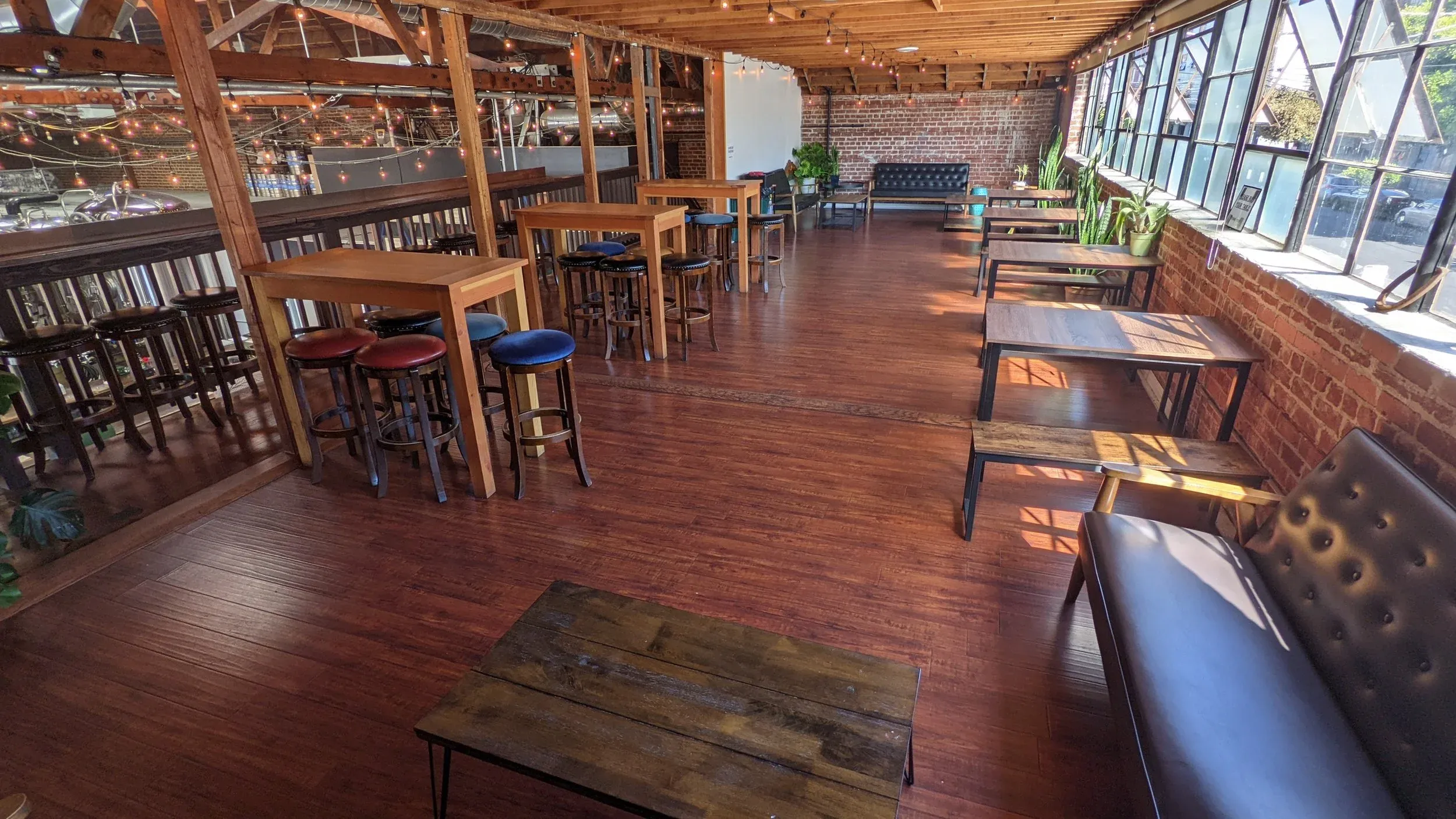 Multi-level room with wooden floors, brick walls, seating, and string lights.