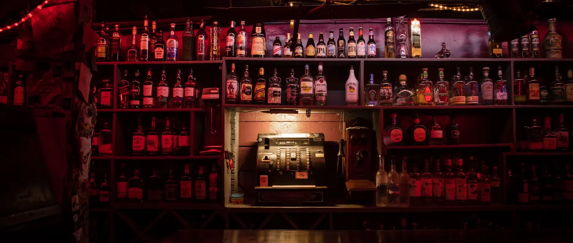 Vintage cash register and liquor bottles on dark bar shelves.