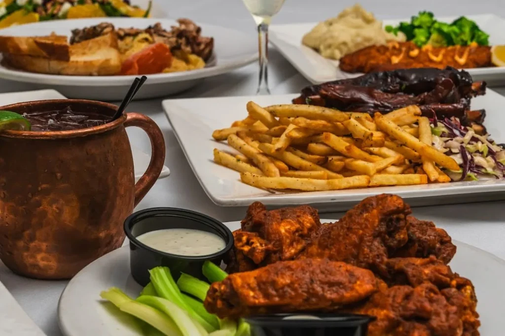 Several plates of restaurant food, including wings, ribs, and fries.