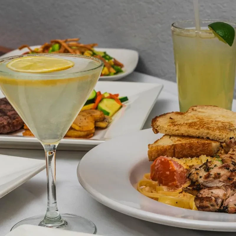 A table with several food plates and two alcoholic beverages.