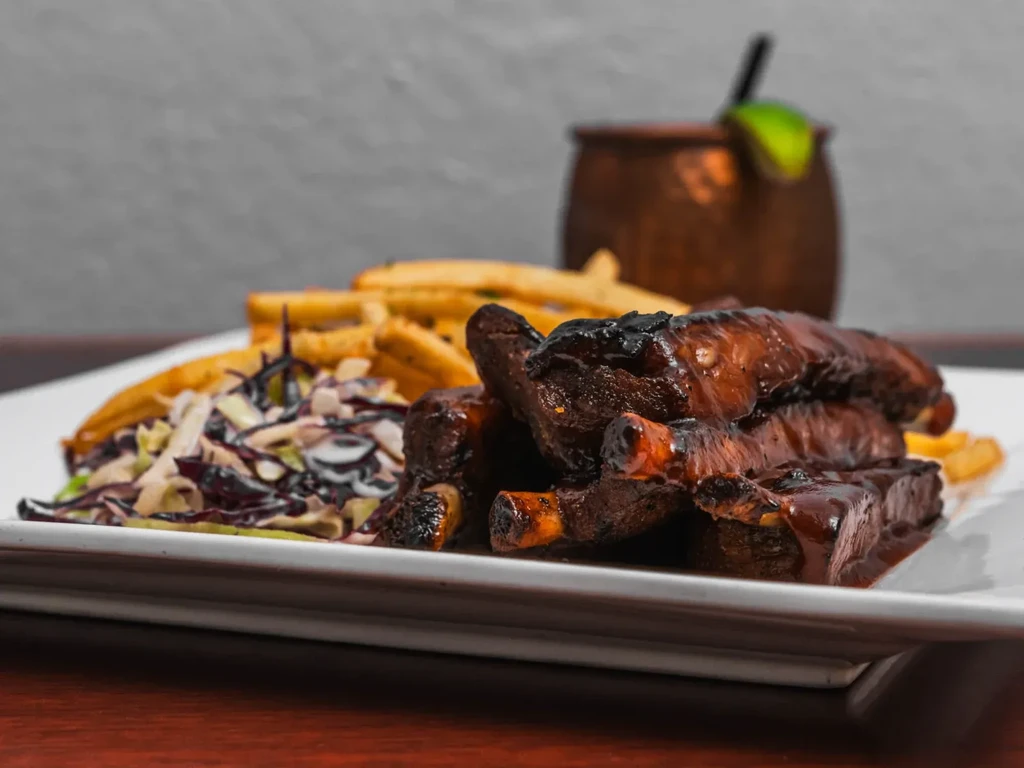 Platter of BBQ ribs, fries, coleslaw, and a cocktail.