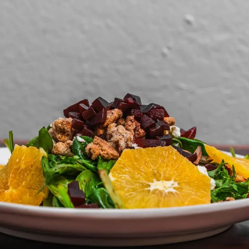 A salad with spinach, orange slices, beets, and candied nuts.