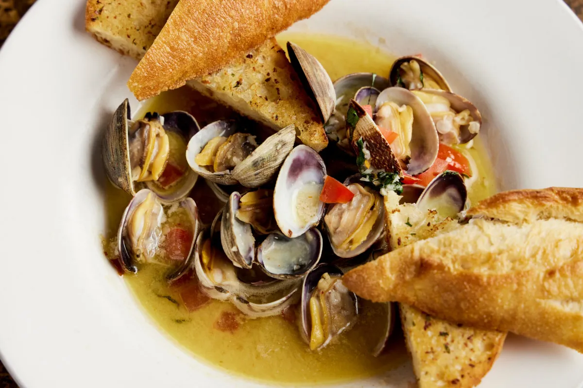 Bowl of clams in broth, with diced tomatoes and toasted bread.