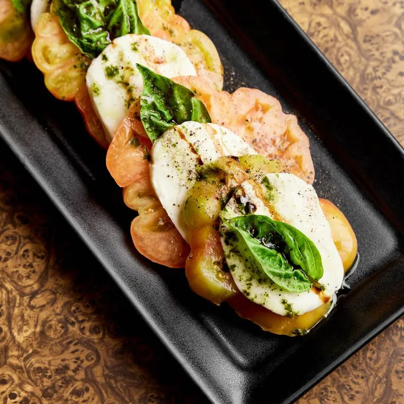 Caprese salad with sliced tomatoes, mozzarella, basil, and pesto.