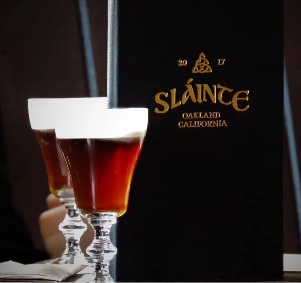 Two Irish coffees in stemmed glasses next to a Sláinte sign.