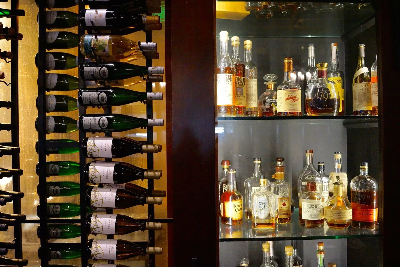 Wine bottles on racks and various spirits displayed in a glass case.