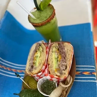 A cut sandwich, green drink, and pickles on a blue mat.