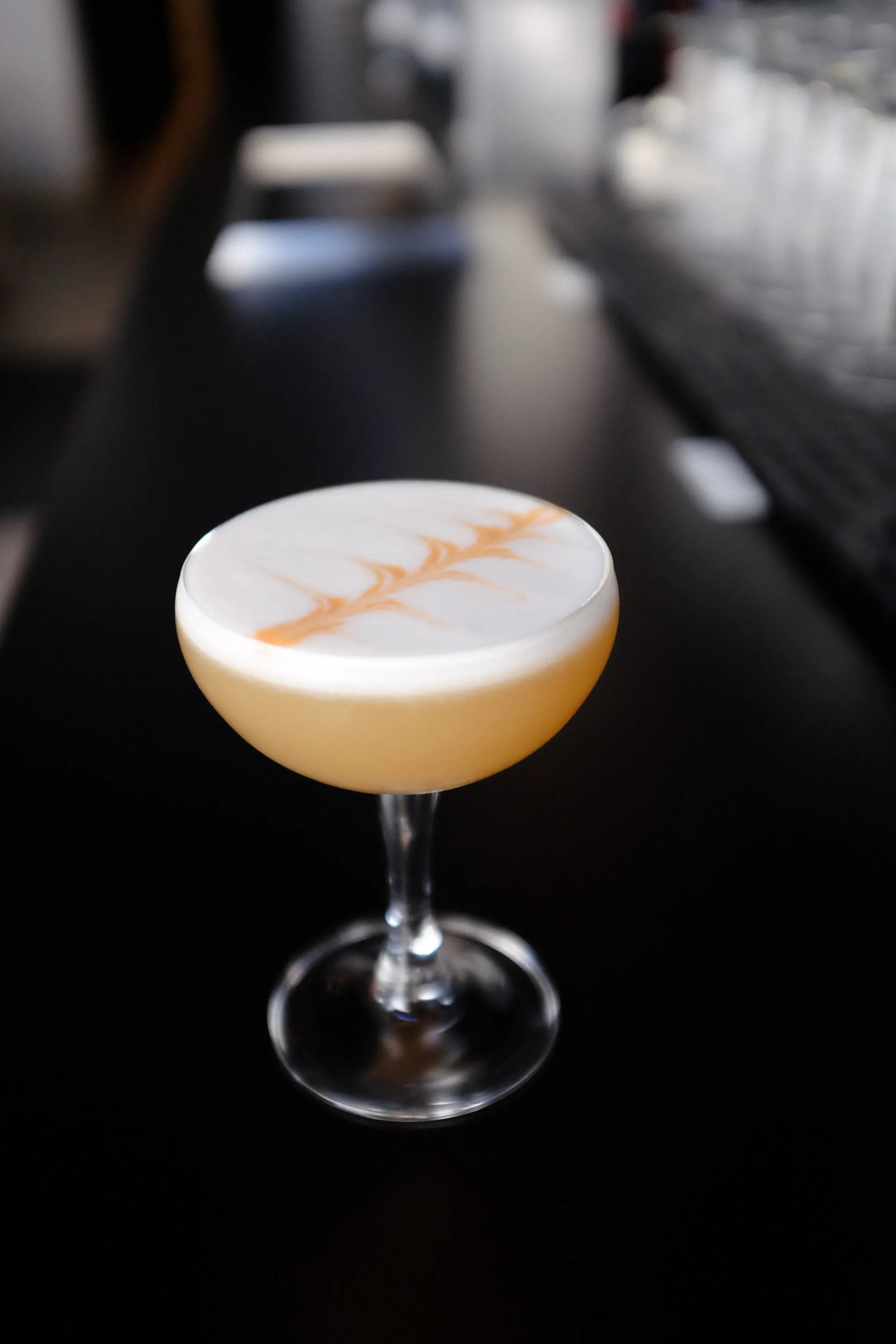 Cocktail in a coupe glass with white foam and orange pattern.