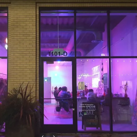 Storefront with "1101-D", people inside a purple-lit space.