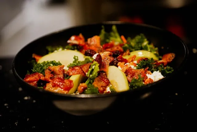Salad with leafy greens, apple slices, bacon, cheese, and dried fruit.