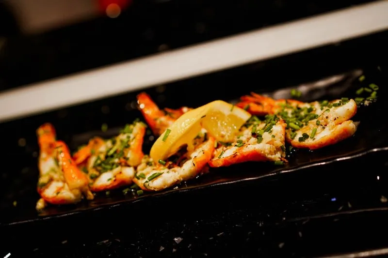 Cooked shrimp with lemon and chives on a dark plate.