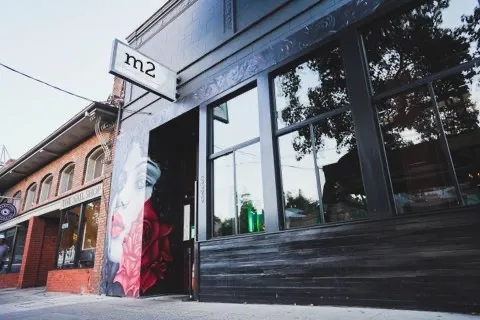 Black building with 'm2' sign, mural of a woman, and red roses.