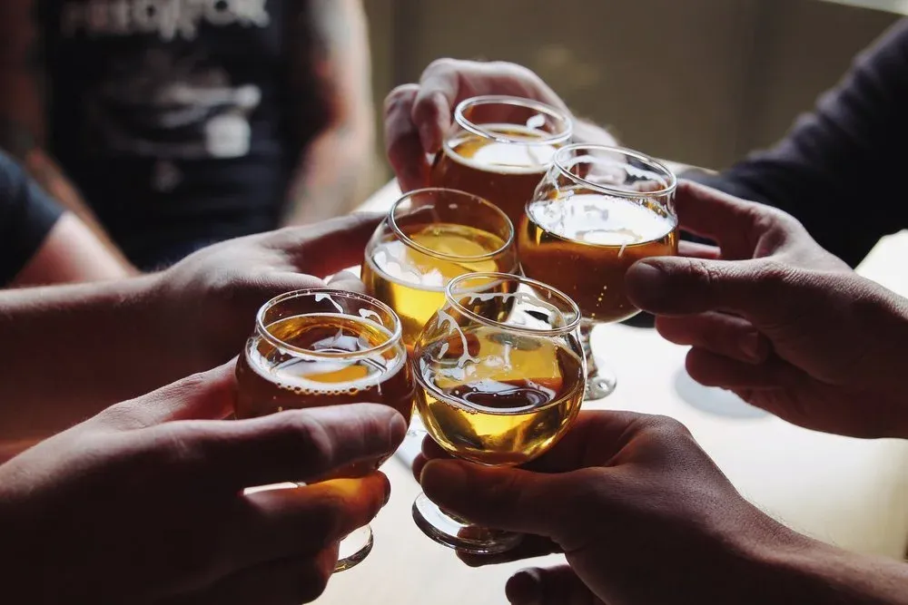 Five hands holding small glasses filled with amber liquid.