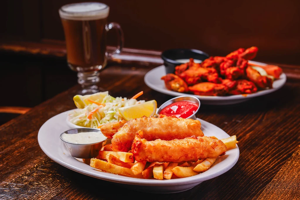 Fish and chips, coleslaw, and drinks on a wooden table.