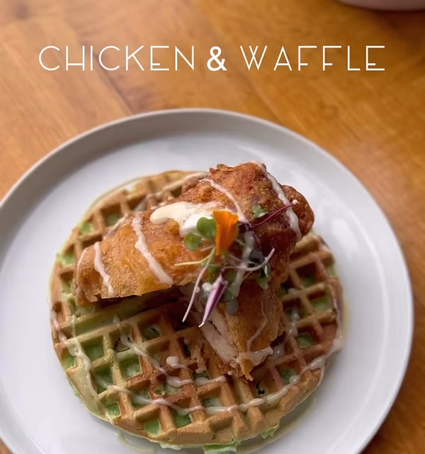 Fried chicken and green waffle, drizzled with sauce and microgreens.