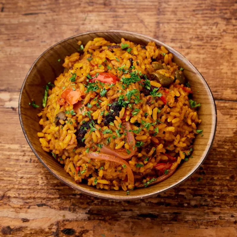 Orange rice with peppers, onions, and parsley in a wooden bowl.