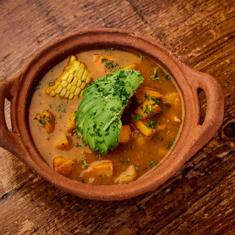 Stew with corn, avocado, and sweet potato in a terracotta bowl.