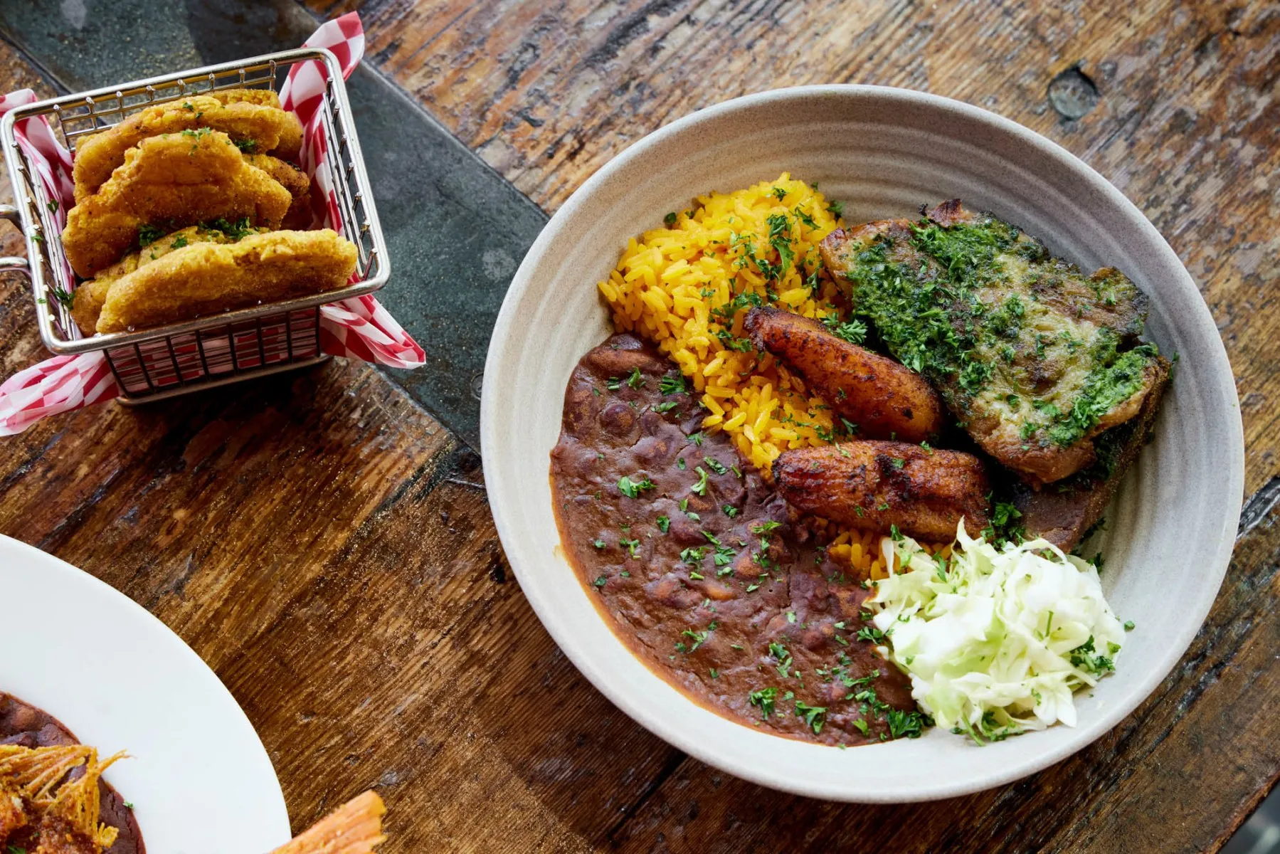 Bowl of yellow rice, black beans, fried plantains, meat, and fried side.