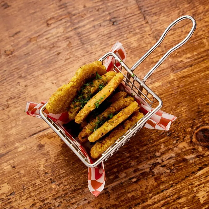 Fried pickles in a metal basket with checkered paper on wood.