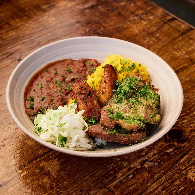 Bowl with beans, yellow rice, fried plantains, meat, and shredded cabbage.