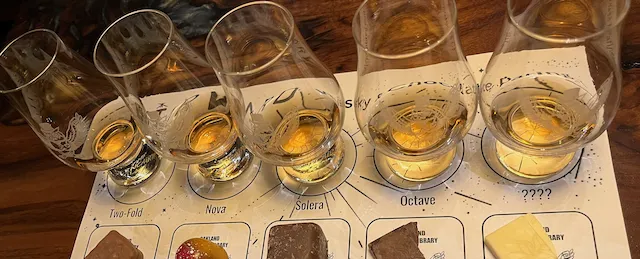 Five snifter glasses of spirits and food pairings on a mat.