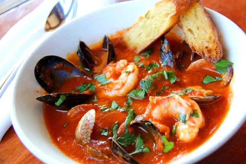 A bowl of seafood cioppino with mussels, shrimp, clams, and toast.