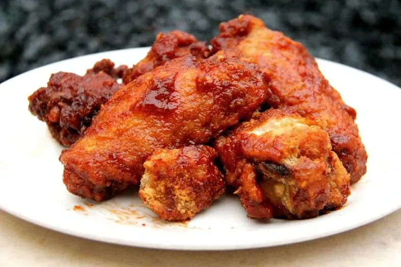 Several brown, saucy chicken wings on a white plate.