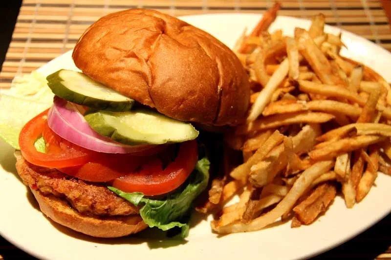 A hamburger with lettuce, tomato, onion, and pickles, with a side of fries.