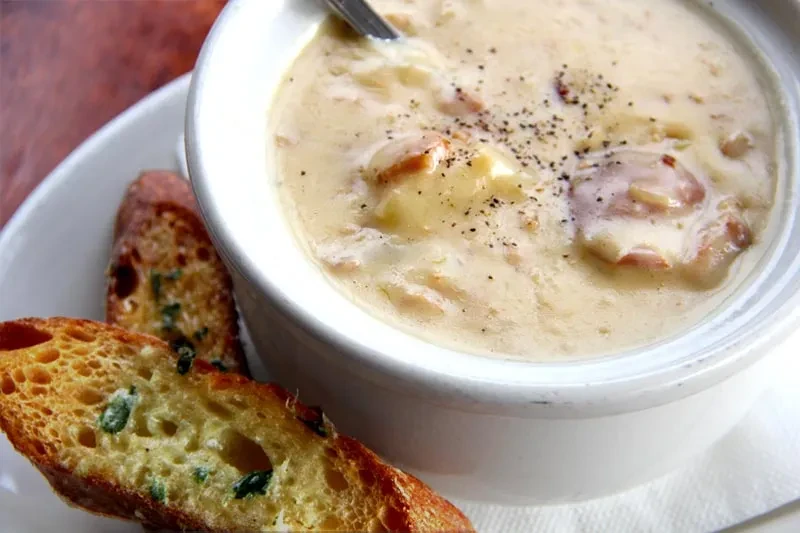 A bowl of creamy clam chowder with black pepper and garlic bread.
