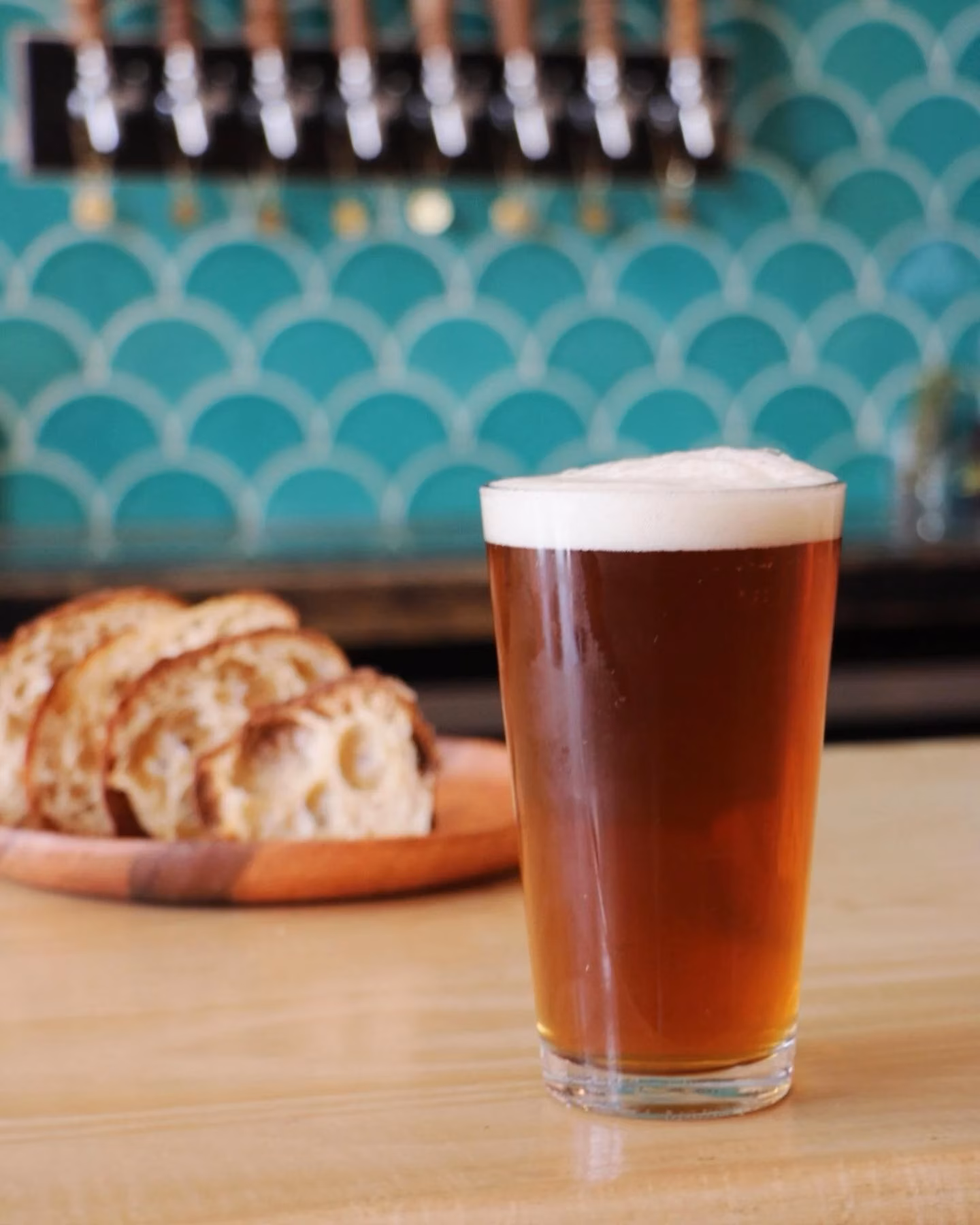Pint of beer with foam and sliced bread on a bar.