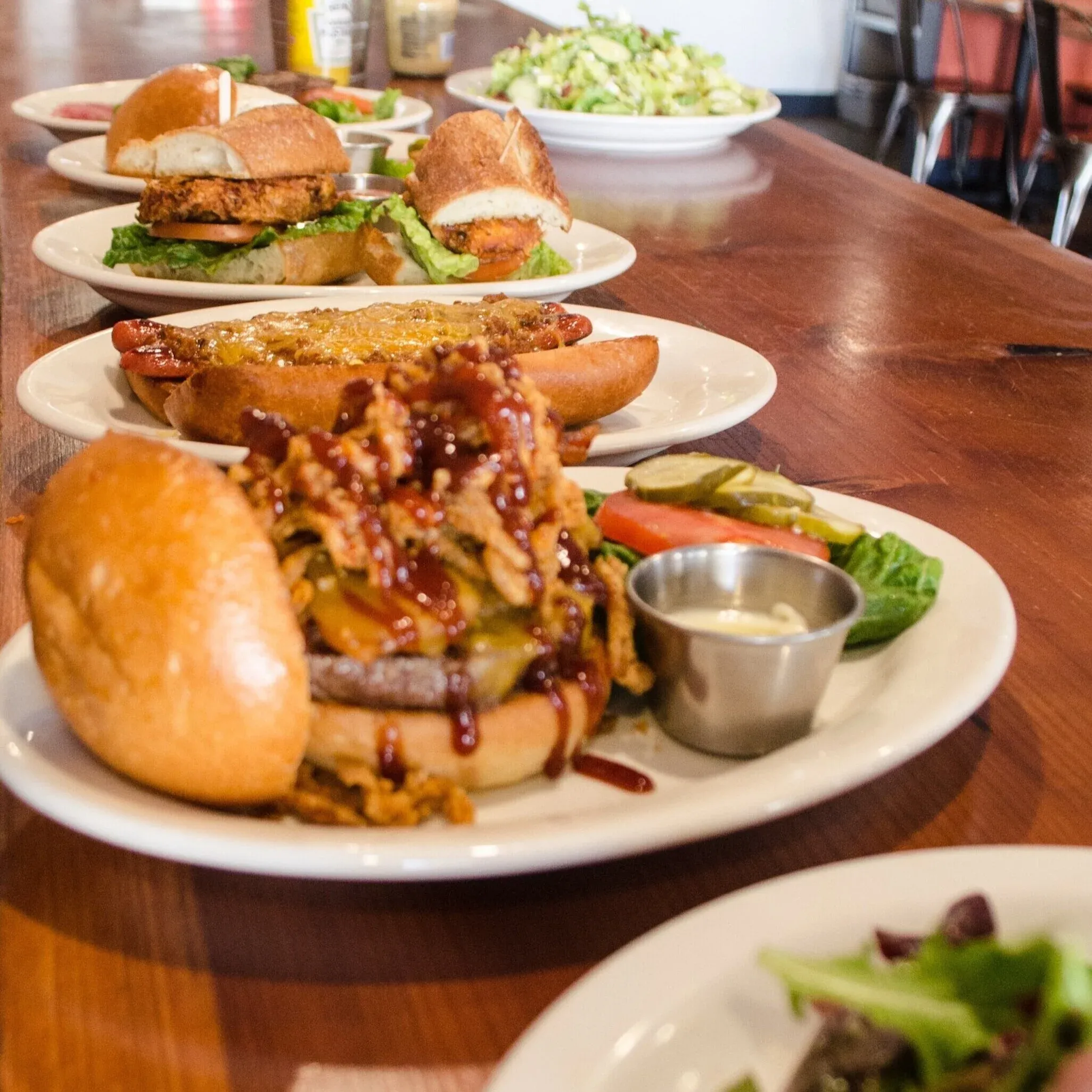 Several plates of burgers, hot dog, chicken sandwich, and salad.