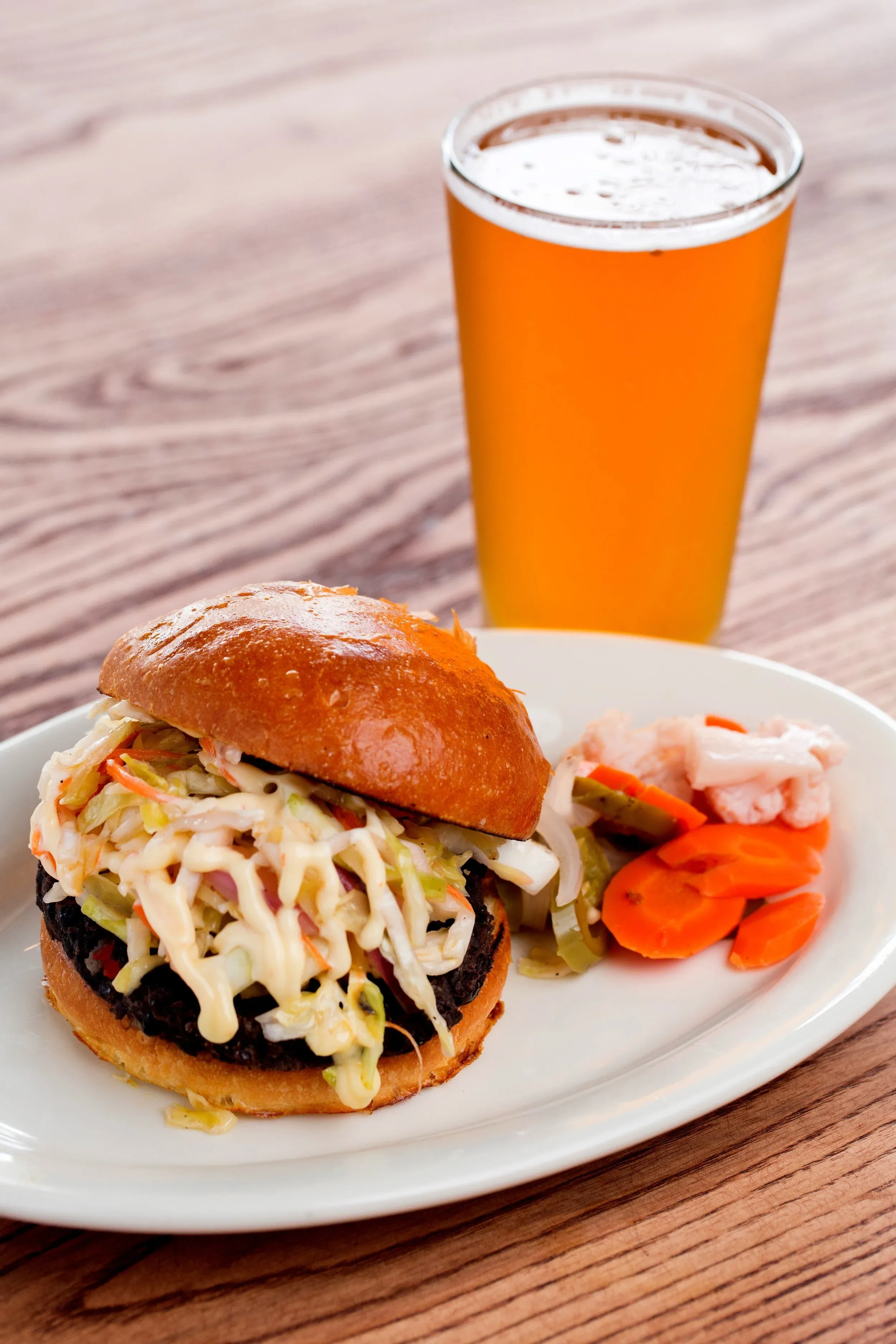 Burger with coleslaw, pickled vegetables, and a glass of beer.