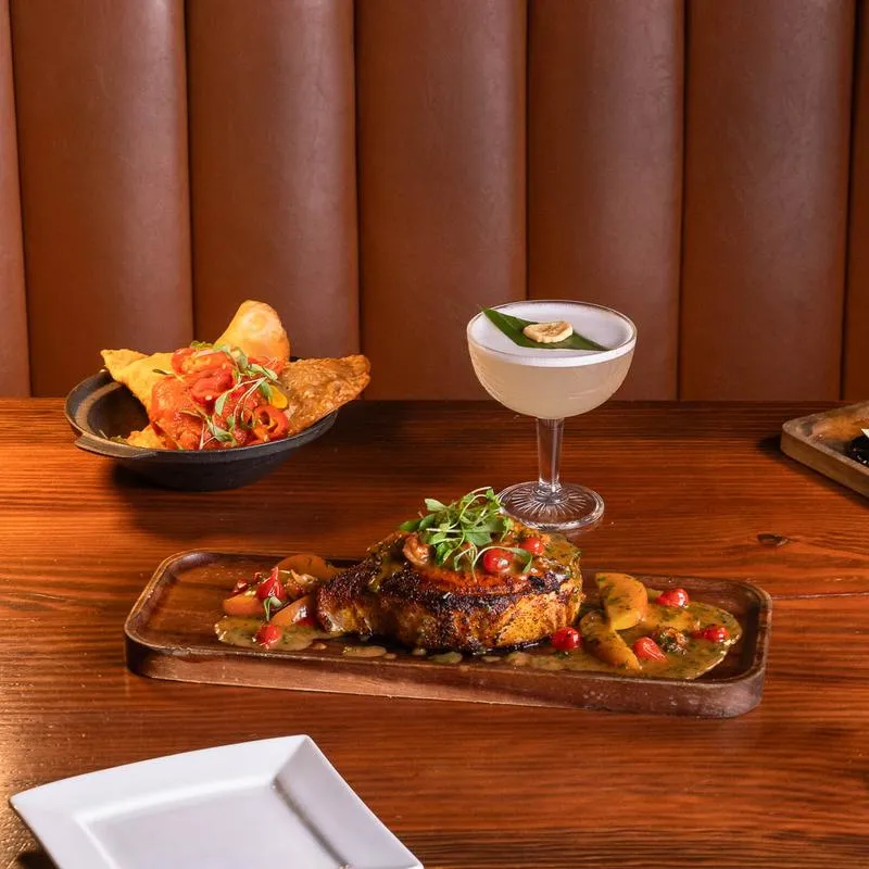 Steak, cocktail, and fried pastries on a wooden table.