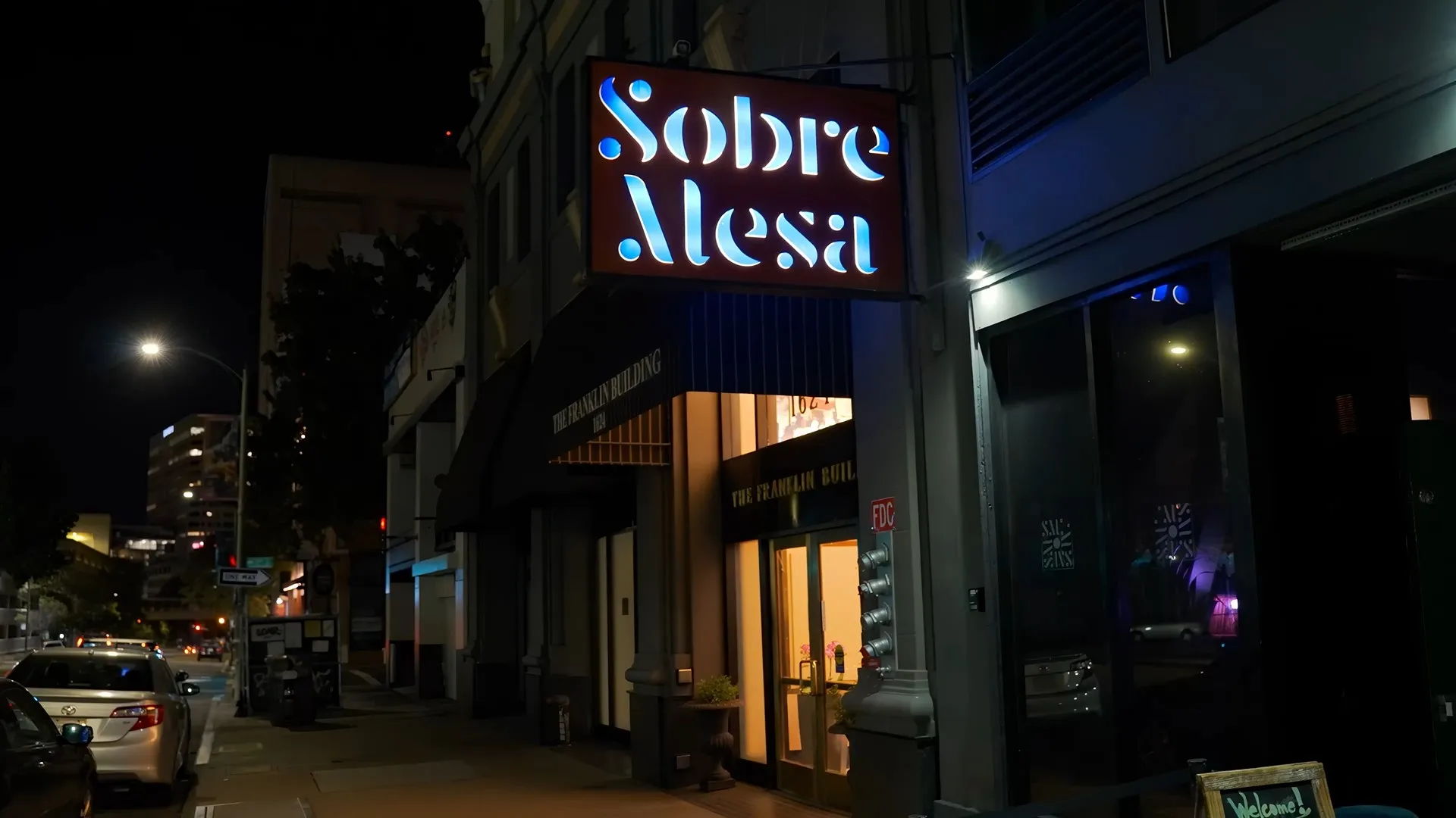 Illuminated 'Sobre Mesa' sign on The Franklin Building at night.